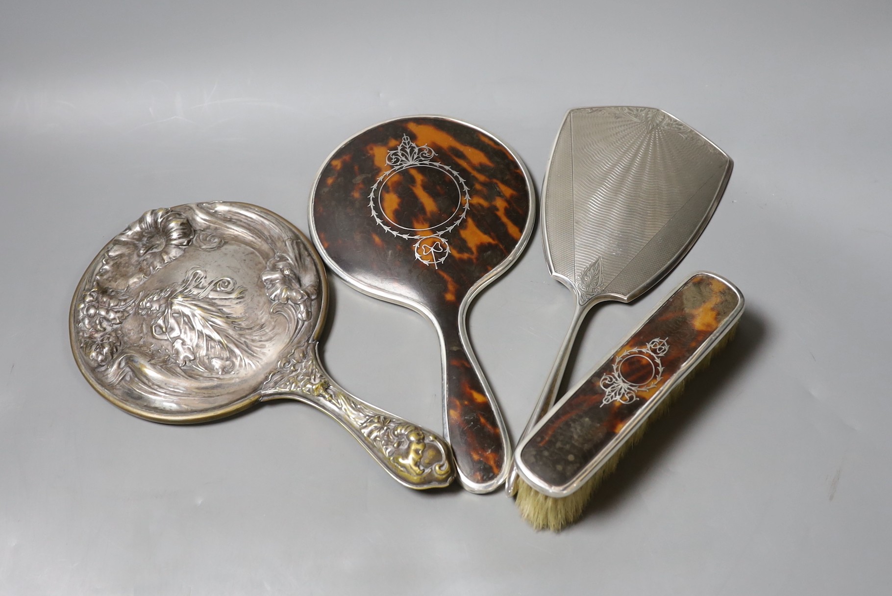 A George V silver and tortoiseshell mounted hand mirror and clothes brush, one other silver mounted hand mirror and a plated hand mirror.